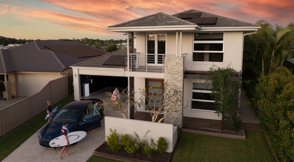 A family on their driveway with their tesla at home charging station.