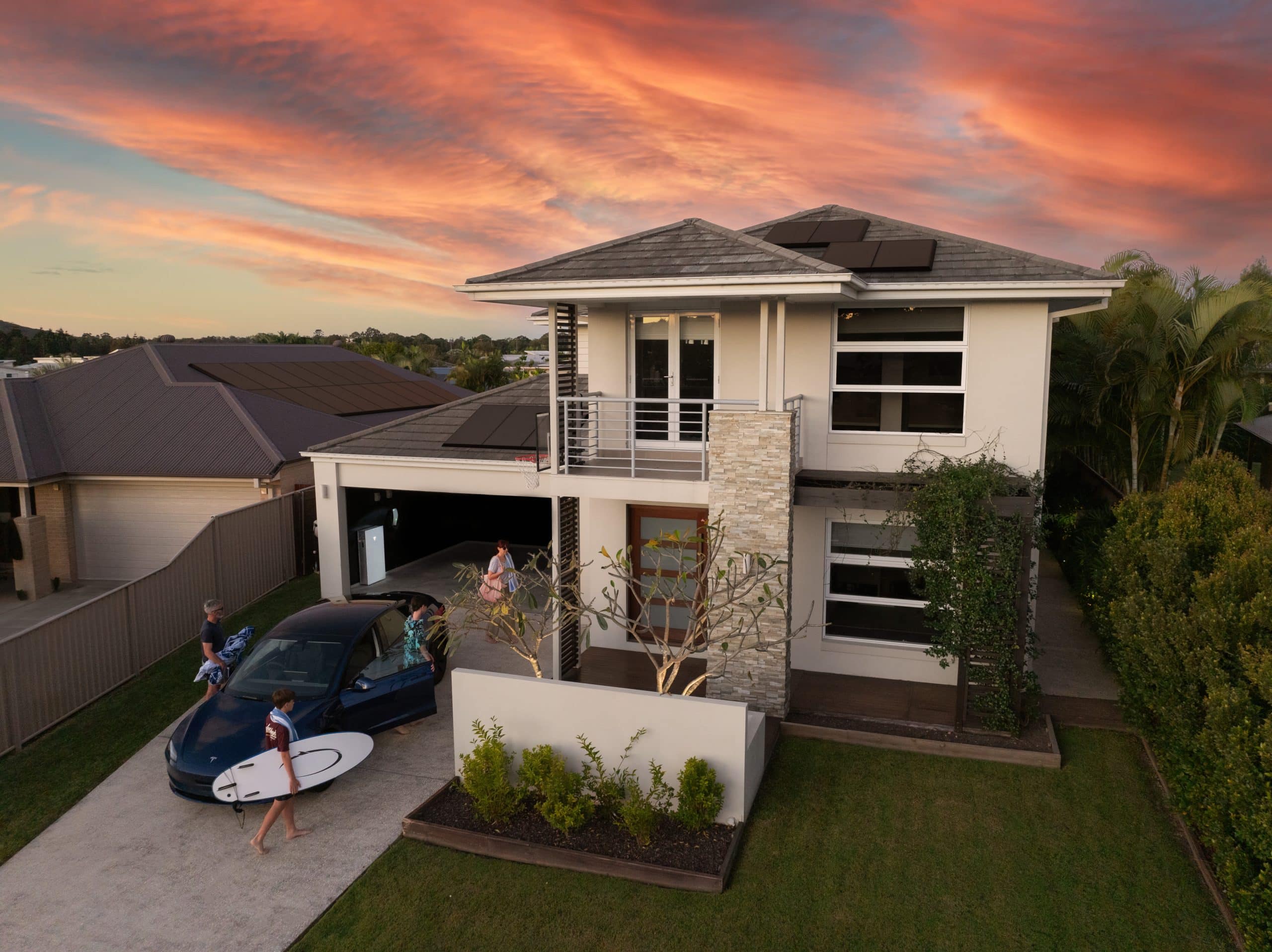 A family on their driveway with their tesla at home charging station.